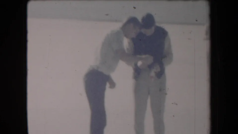 Two men remain focused on an object in a sun-bleached 1958 Arizona home-movie frame with soft focus and faded color.
