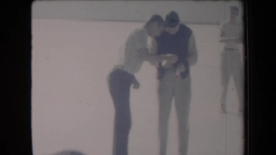 1958 Arizona home-movie frame showing teens on a pale salt flat, with two figures bent toward a football and another standing nearby.