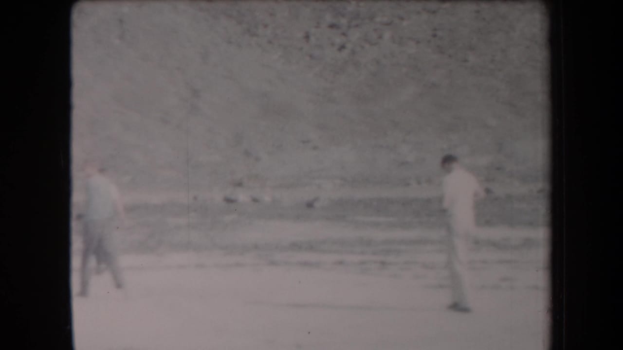 Distant young men walk through a sparse sandy desert setting in Arizona, filmed on 8mm in 1958.