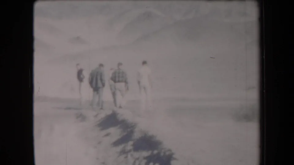 1958 Arizona 8mm frame showing adult men walking away across a washed-out desert landscape toward distant mountains.