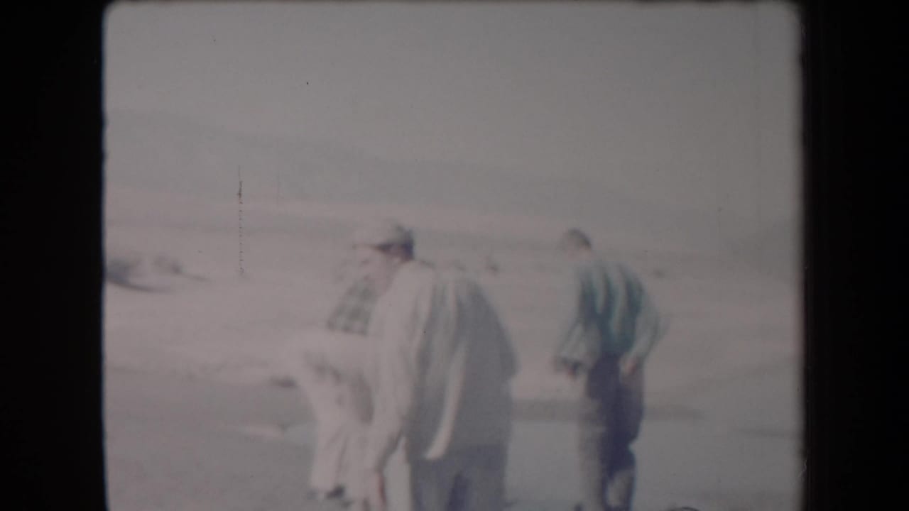 Adult men, one in a light suit and hat, stand together in an Arizona desert setting in 1958 home-movie footage.