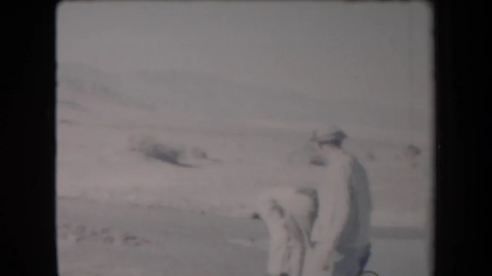 1958 Arizona home-movie frame with two adult men paused near scrub in an open desert landscape.