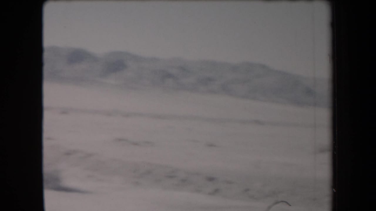1958 Arizona 8mm frame showing a pale desert landscape and soft mountain ridge in the distance.