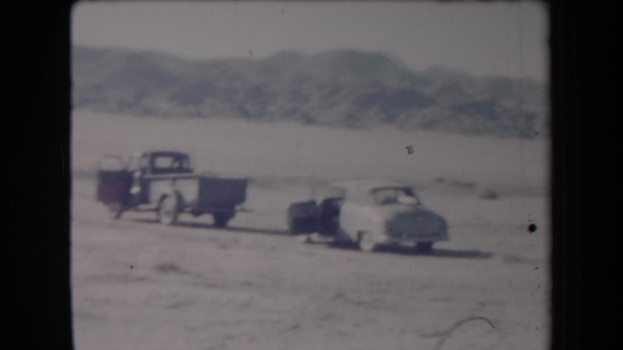 1958 Arizona roadside stop with a pickup, small trailer, and light-colored car parked on open desert ground.