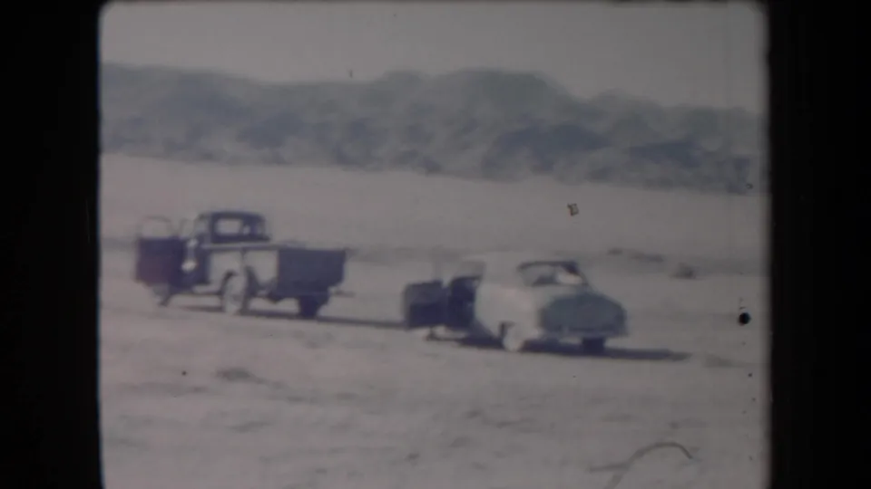 1958 Arizona roadside stop with a pickup, small trailer, and light-colored car parked on open desert ground.