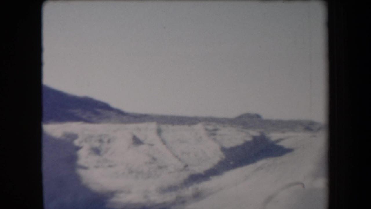Desert roadside and low hills seen from a moving vehicle beside a highway.