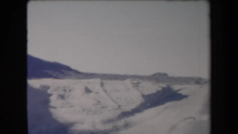 1958 Arizona home-movie frame showing a pale desert roadside, low hills, and hazy sky from a moving road-trip viewpoint.