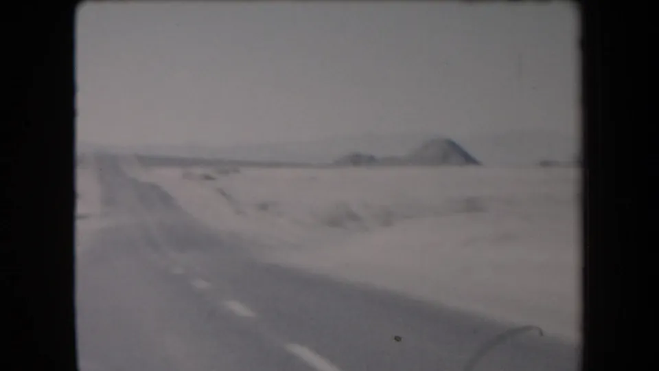 1958 Arizona home-movie frame showing a soft, moving view of a road edge, flat desert, and distant low mountain forms.
