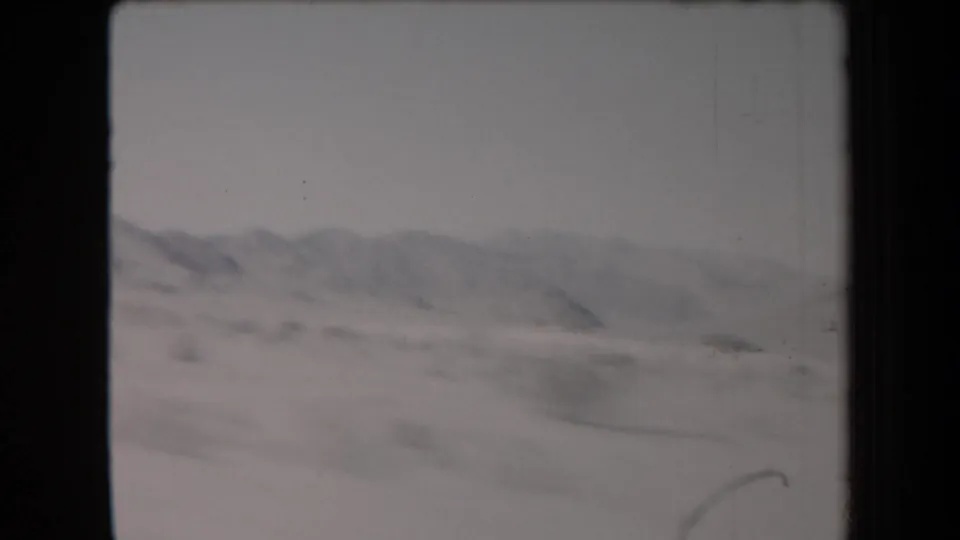 1958 Arizona desert road-trip frame with low mountain ridges, open scrubland, and soft motion blur from travel.