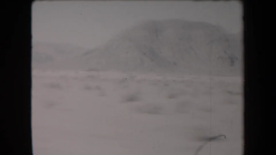 1958 Arizona home-movie frame showing a hazy desert ridge beyond open terrain, recorded from a moving road-trip viewpoint.