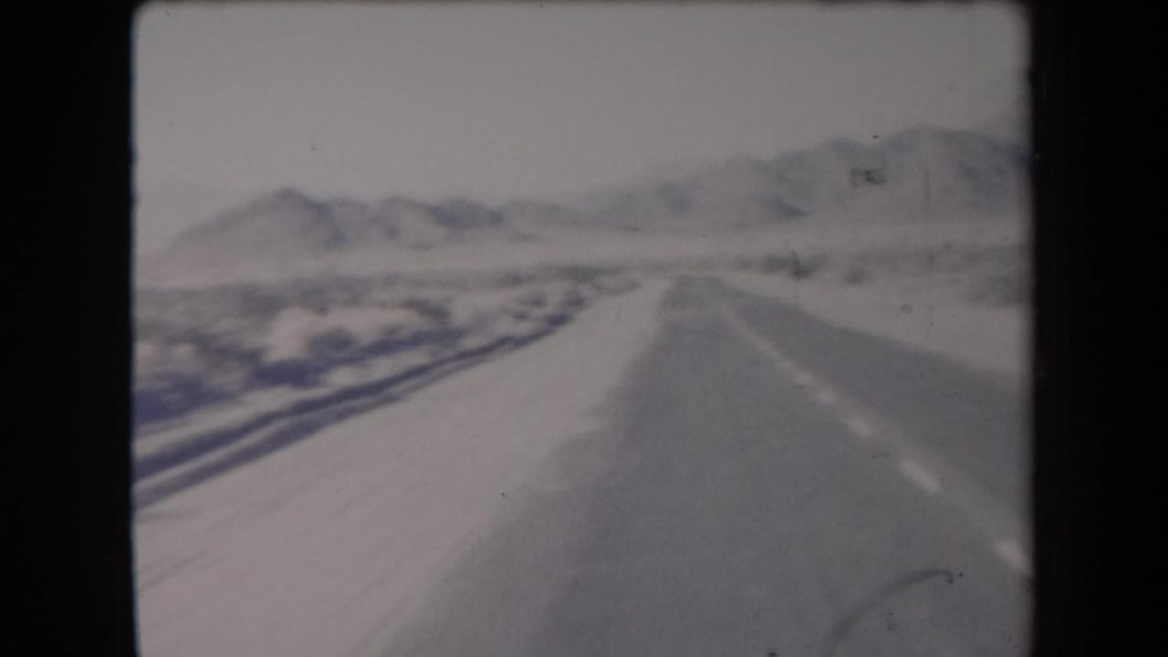 Snowy paved road receding toward distant mountains in a desert landscape.