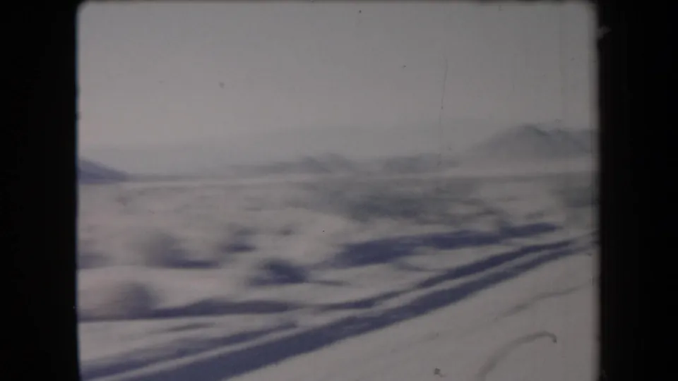 1958 Arizona road-trip frame looking across snow-dusted desert brush toward low mountains from a moving vehicle.