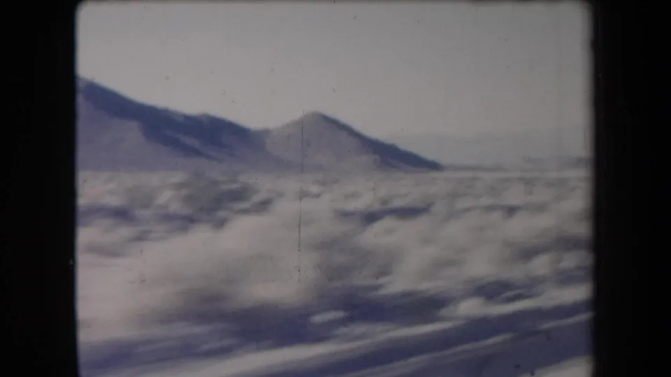 1958 Arizona home-movie view of a snowy desert plain with a dark mountain slope and blurred roadside foreground.