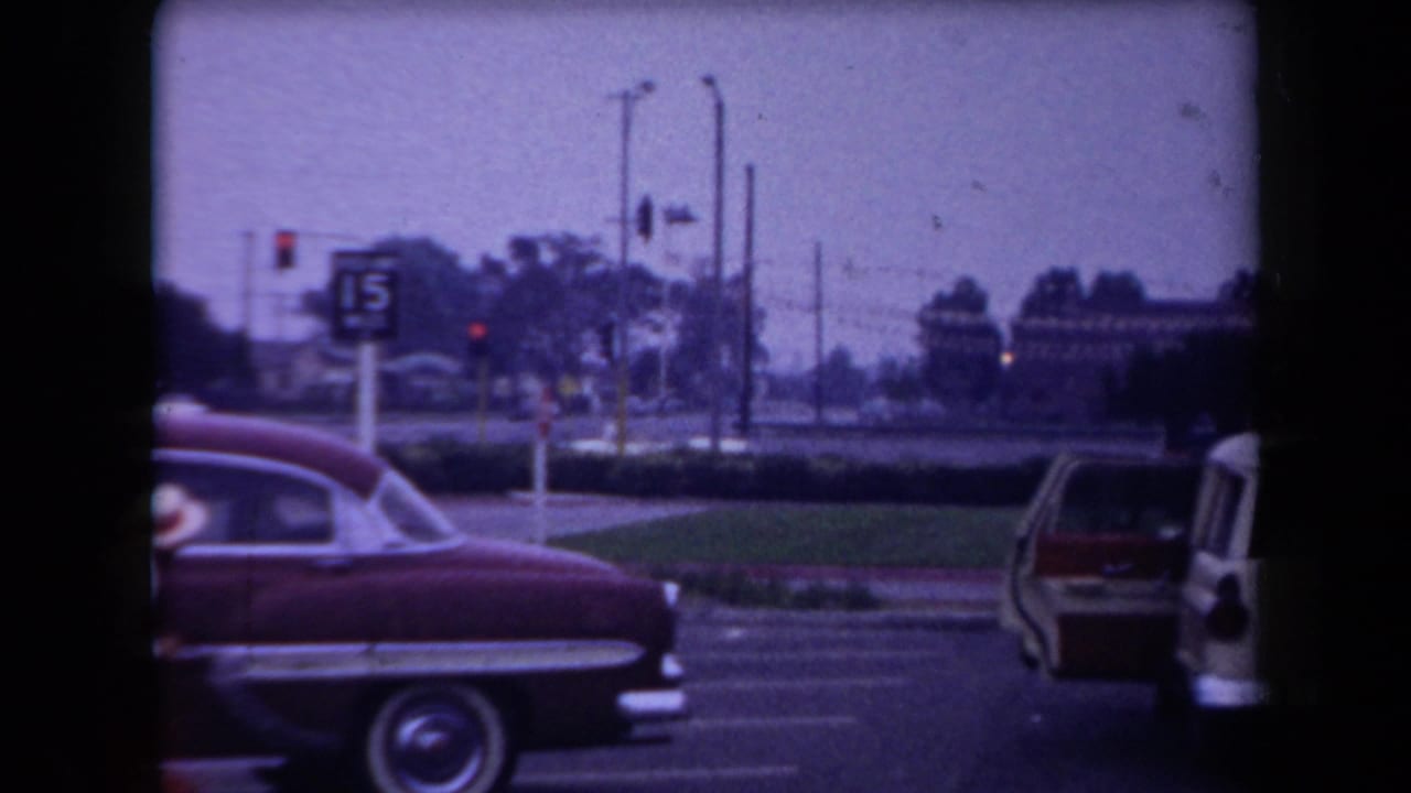 Red mid-century sedan at an Arizona intersection, with traffic lights, utility poles, and a parking sign visible.