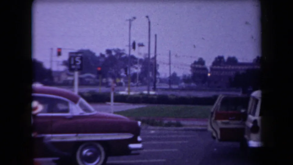 Red mid-century sedan at an Arizona intersection, with traffic lights, utility poles, and a parking sign visible.