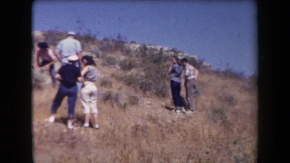 Small family group in 1950s clothing walks and gathers on a dry Arizona hillside under clear sky.