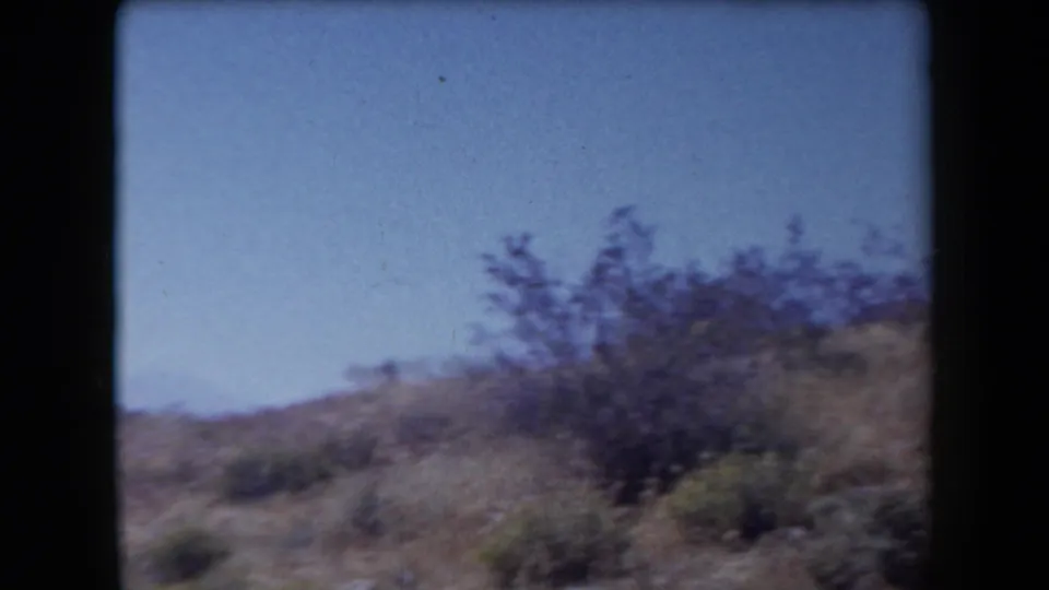 1958 Arizona home-movie frame of sparse shrubs and dry hillside terrain under open sky.