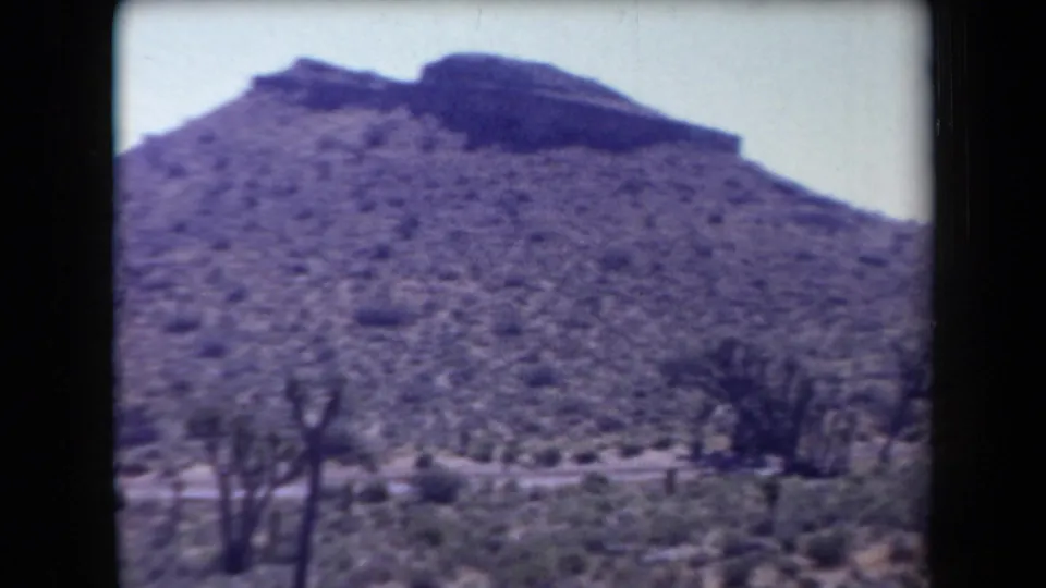 1958 Arizona 8mm frame showing a rugged desert hillside, Joshua trees, scrub, and a pale sky.