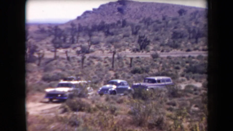 1958 Arizona desert roadside scene showing three mid-century cars parked below hills and Joshua trees.