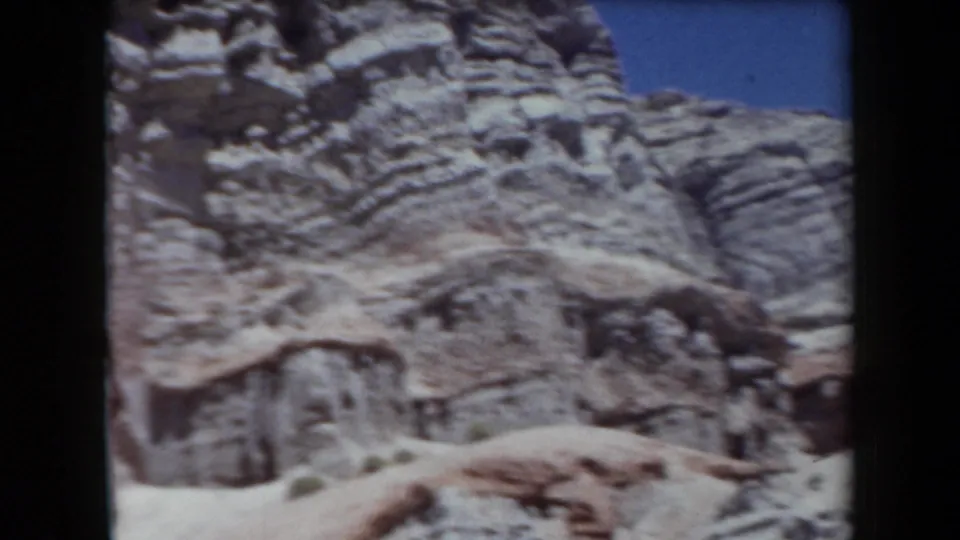 1958 Arizona 8mm frame showing eroded, stratified rock formations under bright blue sky.