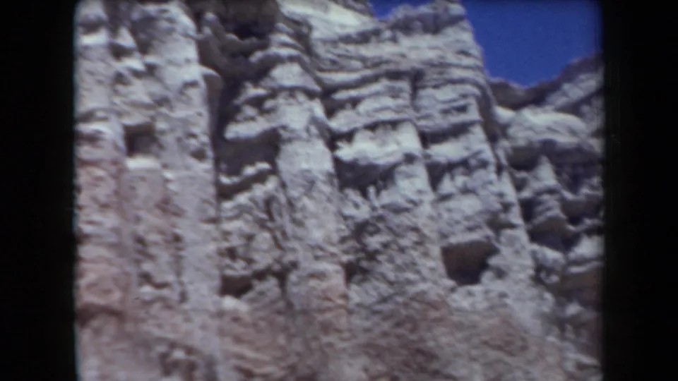 1958 Arizona 8mm close view of a rugged stratified cliff face with weathered pockets and ledges.