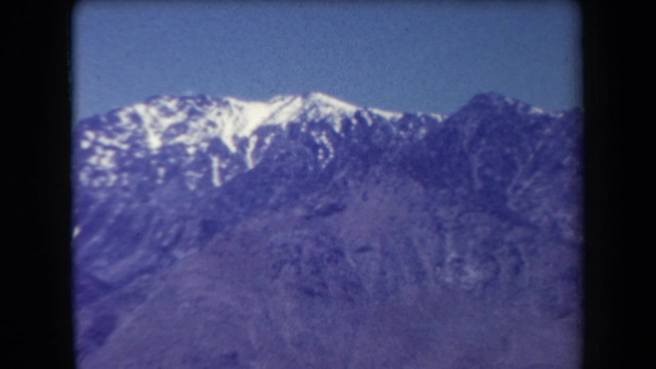 Distant mountain ridge with snow patches, blue sky, and visible film gate edges.
