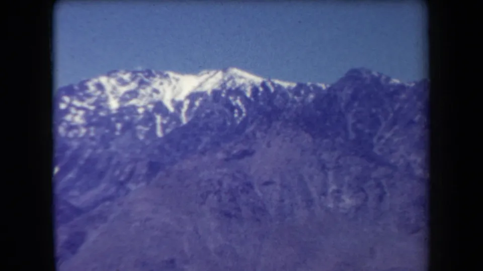 1958 Arizona home-movie frame with a snow-streaked mountain ridge and soft purple-toned foreground slopes.