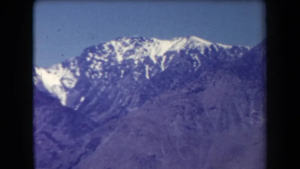 1958 Arizona 8mm still showing a closer section of snow-capped ridge above rugged, purple-hued mountain terrain.