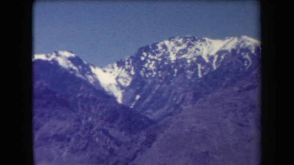1958 Arizona home-movie frame of snow-bright peaks and rugged mountain slopes, with visible film borders and color shift.