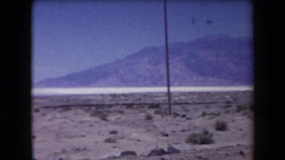 1958 Arizona 8mm view across open desert toward a pale salt-flat band and distant mountains, with a utility pole in the foreground.