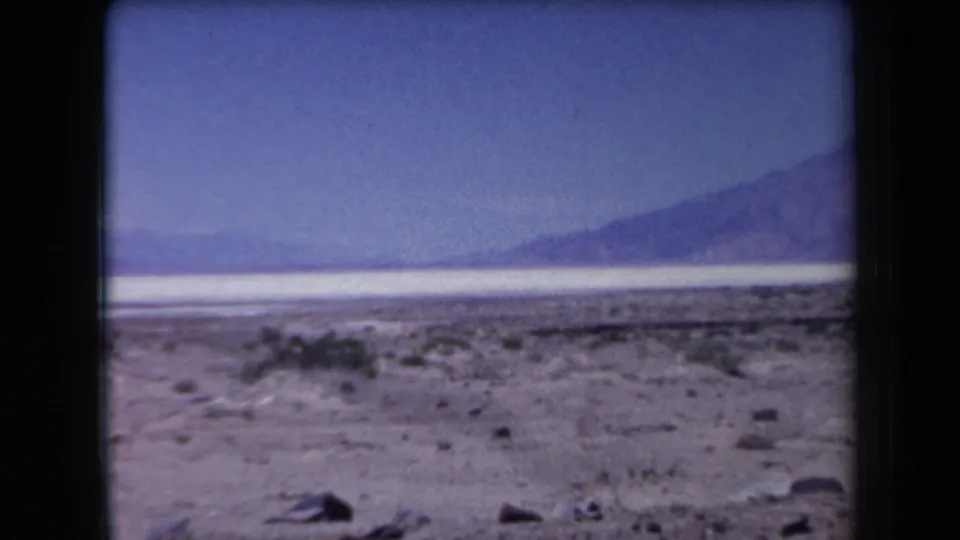1958 Arizona home-movie frame looking across scrubby desert and pale flats toward distant mountain ridges under a clear sky.