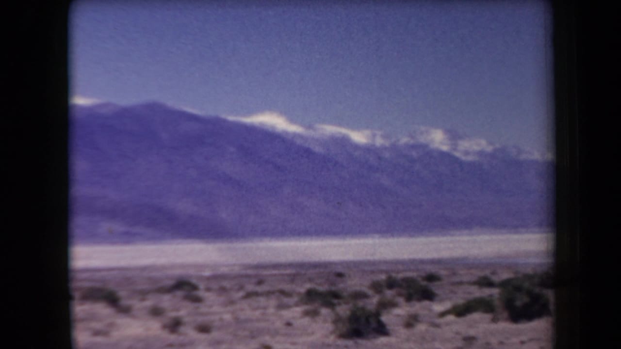 Distant snow-capped mountains beyond scrubby desert flats under a blue sky.