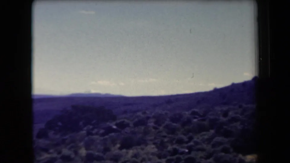 1958 Arizona 8mm frame showing scrub-covered desert hills and distant mountain ridges beneath a pale sky.