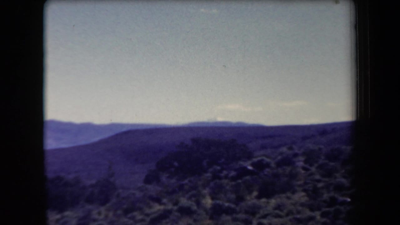 Rolling desert terrain with shrubs and layered mountain ridges in the distance.