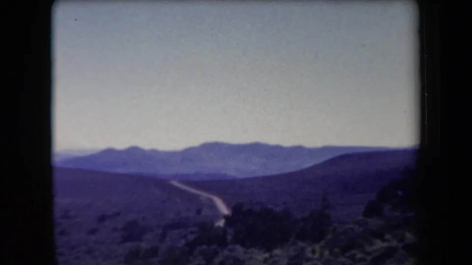 1958 Arizona 8mm frame with a winding dirt road crossing desert hills toward distant mountains.
