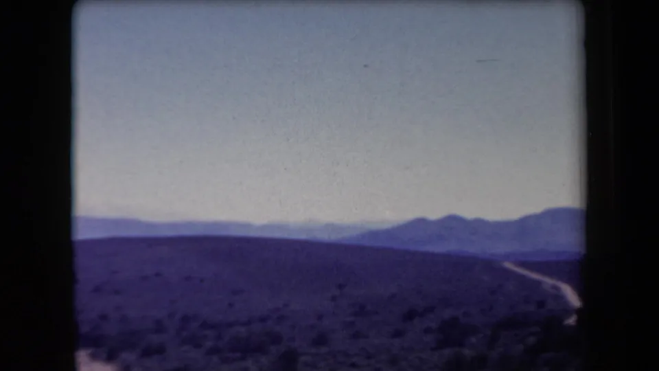 1958 Arizona travel footage frame showing a wide desert hillside, winding road, and distant mountain range.