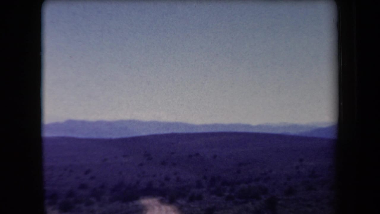 Purple-tinted desert hills and distant mountain ridges beneath a pale sky.