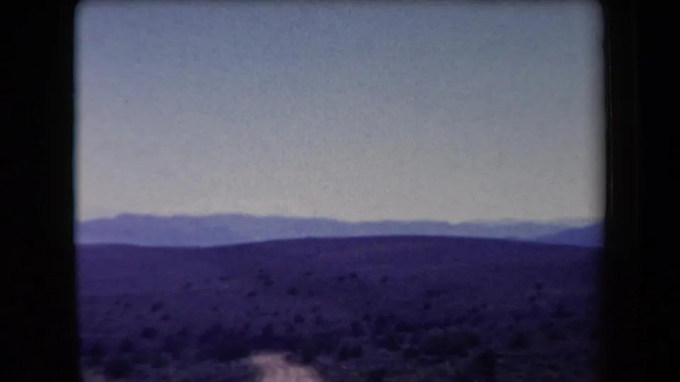 1958 Arizona 8mm frame showing open desert hills and distant mountains with a pale sky and dark film border.