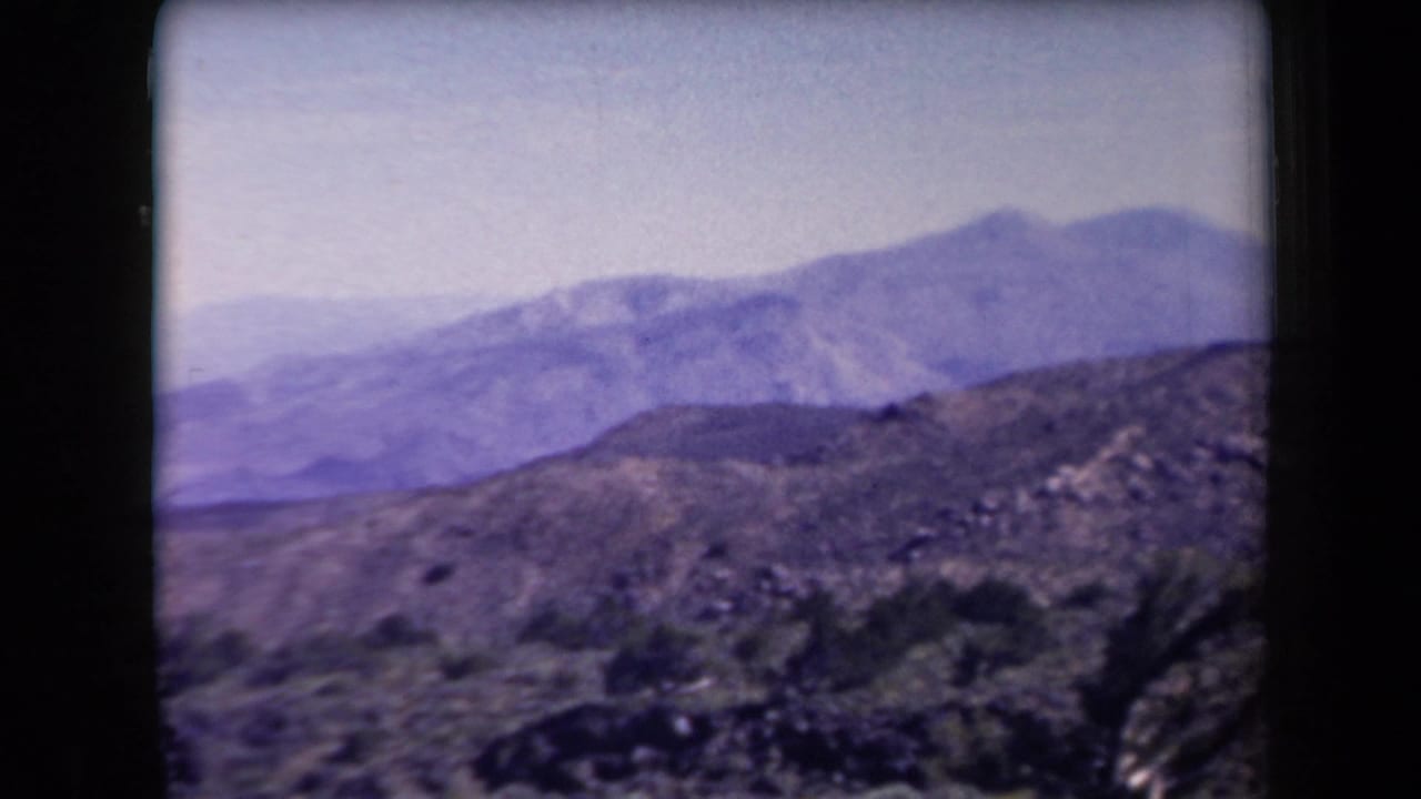 1958 Arizona home-movie view of layered mountain slopes beyond scrubby rocky desert terrain.
