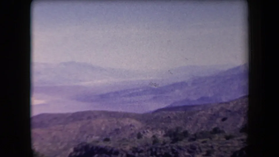1958 Arizona 8mm frame with hazy distant mountains, a basin below, and rocky desert foreground.