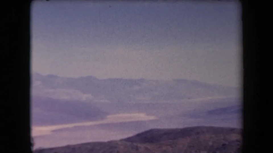 1958 Arizona home-movie frame showing hazy mountain ranges and a low rocky hill under faded blue sky.