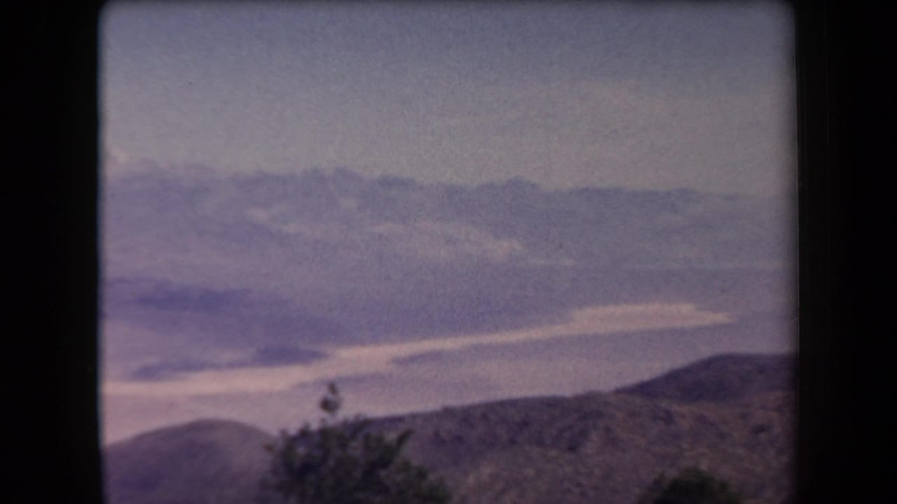 Hazy mountain valley seen from a high overlook with distant pale peaks and dark film borders.