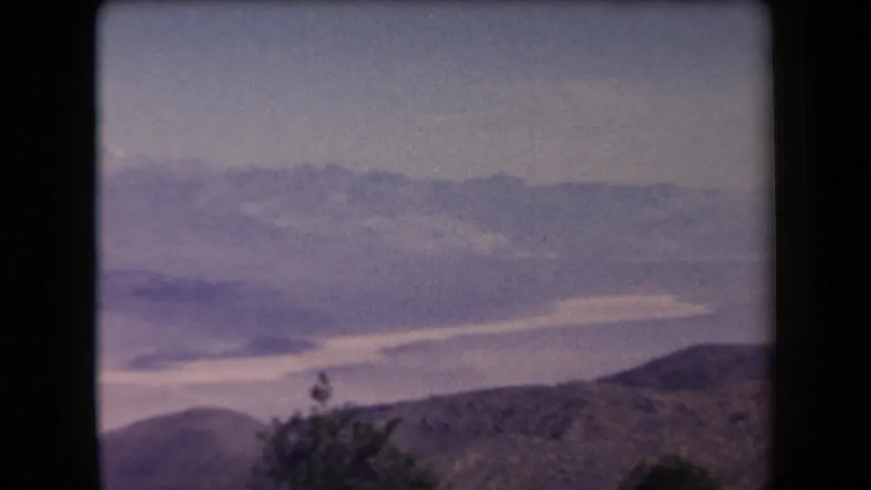 1958 Arizona 8mm frame showing a hazy mountain valley from an elevated viewpoint, with distant pale peaks and scrub in the foreground.
