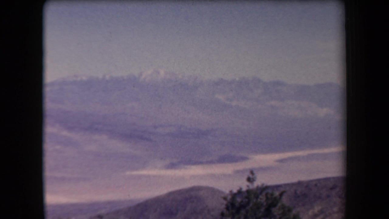 Wide view over a valley toward distant mountains under a hazy sky, with sparse vegetation below.