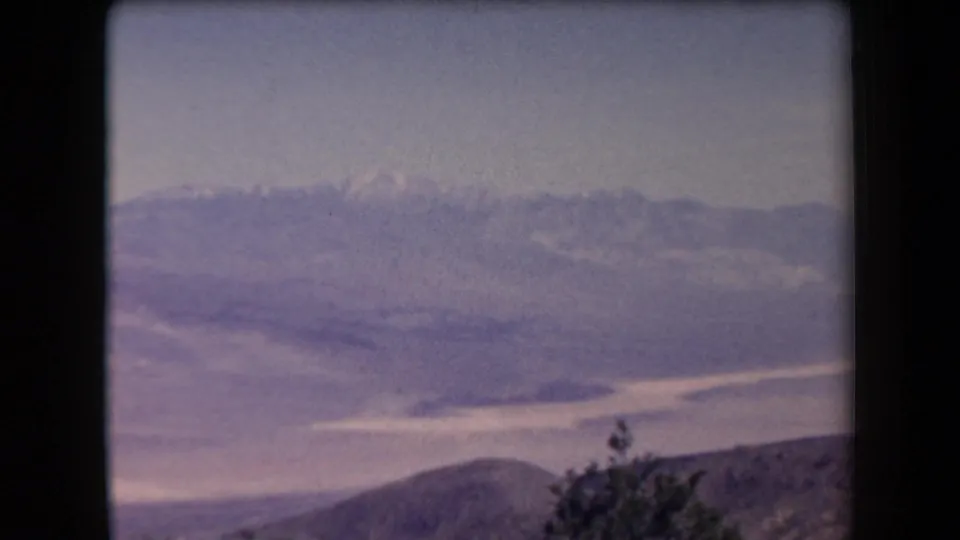 1958 Arizona 8mm frame of a wide mountain vista, looking across a valley toward distant ridges beneath a hazy sky.