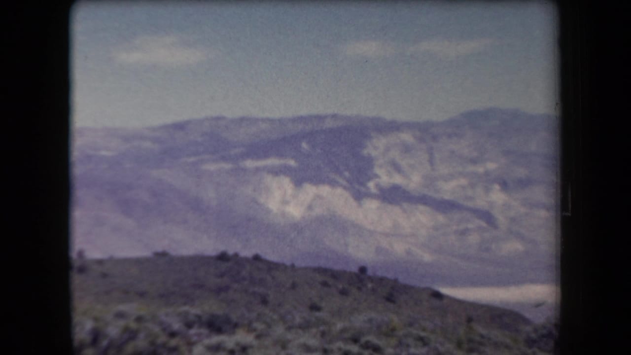 1958 Arizona 8mm frame showing layered desert mountains and scrubland under a pale blue sky.
