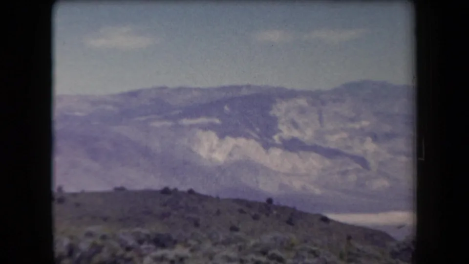 1958 Arizona 8mm frame showing layered desert mountains and scrubland under a pale blue sky.