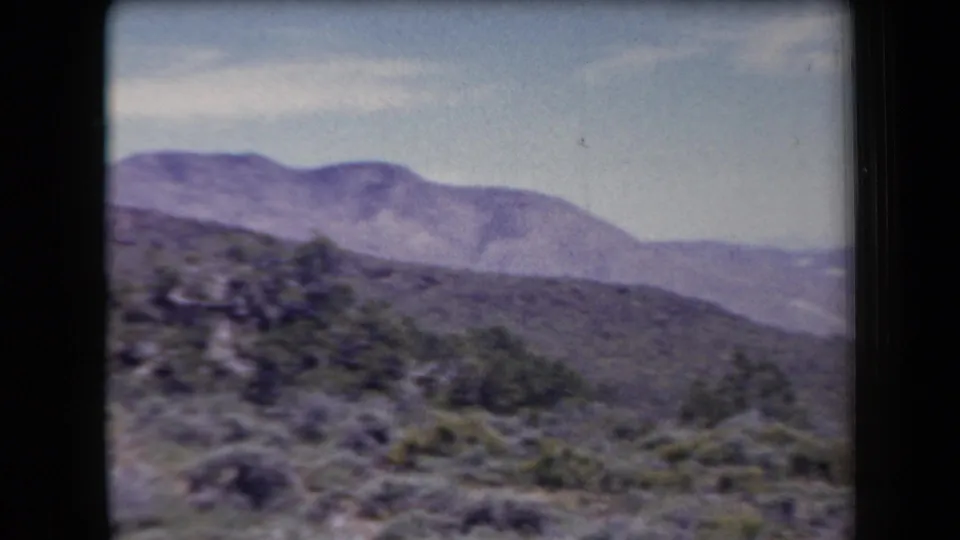 1958 Arizona 8mm landscape frame with low desert vegetation and rounded mountains beyond.