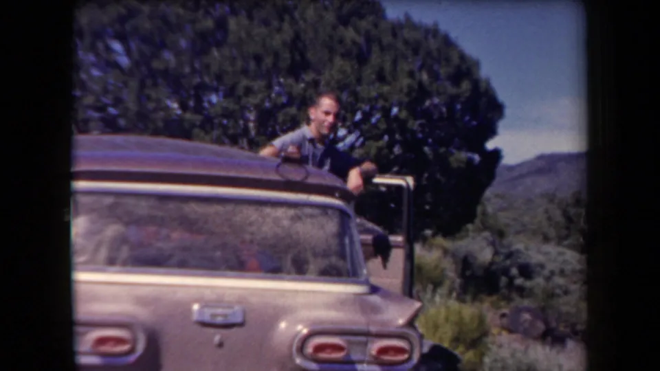 1958 Arizona home-movie frame showing an adult man beside a parked 1950s station wagon near a large tree.