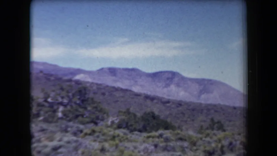 Arizona 1958 landscape frame with scrub vegetation, scattered trees, and a broad low mountain ridge in the distance.